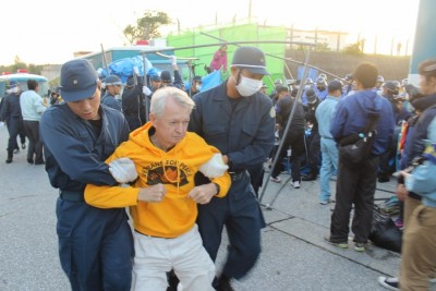 A VFP member being dragged by both arms to the confinement area surrounded by iron fencing and riot police vehicles at 7:24 a.m. on December 11 in Henoko, Nago
